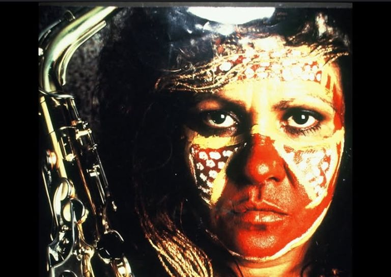 Close-up portrait of Indigenous Australian blues musician Marlene Cummins with traditional face paint, holding a saxophone.